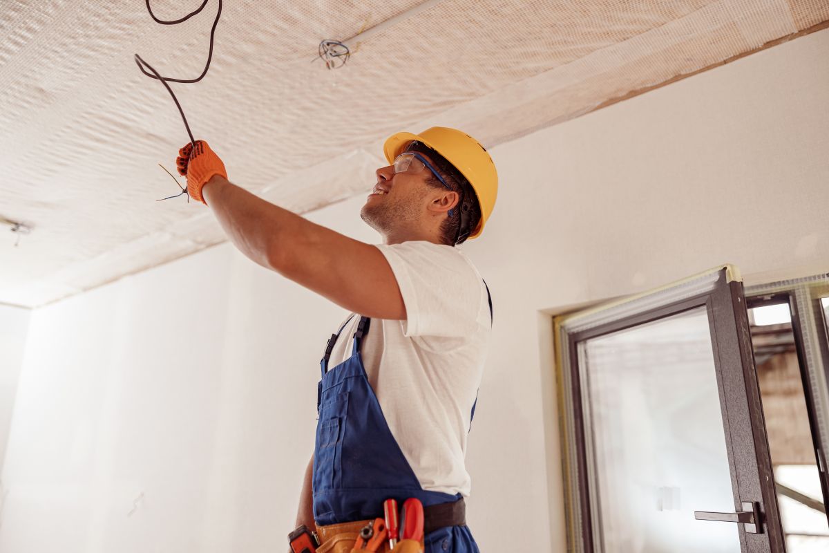 Cheerful young man in safety helmet looking at ceiling and smiling while holding electrical wire